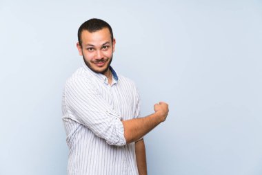 Izole mavi duvar üzerinde Kolombiyalı adam geri işaret