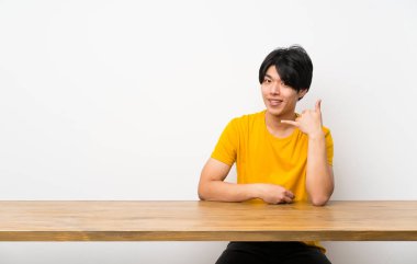 Sarı gömlekli Asyalı adam telefon jesti yapıyor. Beni geri arayın işareti