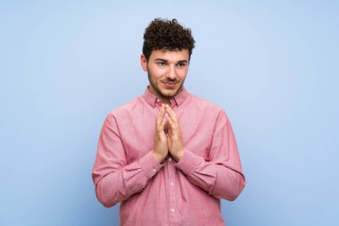 İzole mavi duvar üzerinde kıvırcık saçlı adam bir şey entrika