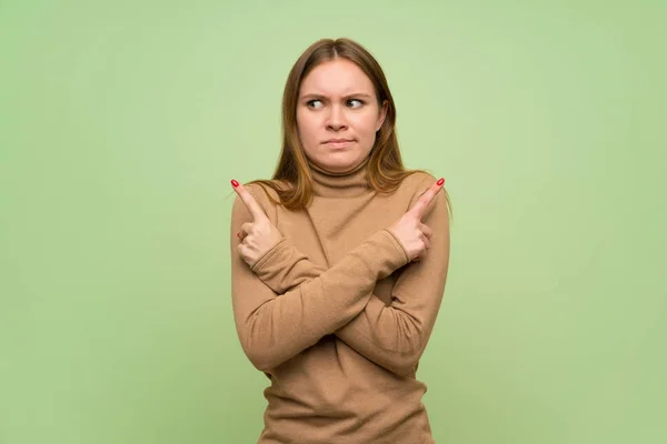 Young woman with turtleneck sweater pointing to the laterals having doubts