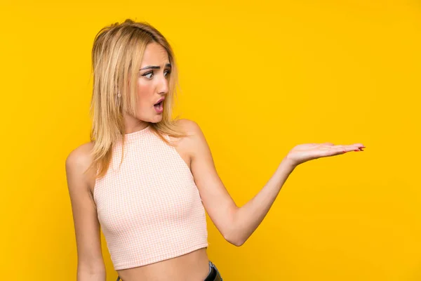 Young Blonde Woman Isolated Yellow Wall Holding Copyspace Imaginary Palm — Stock Photo, Image