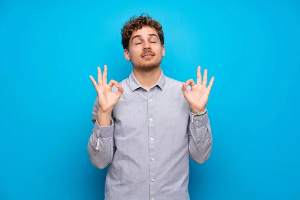 Blonde man over blue wall in zen pose