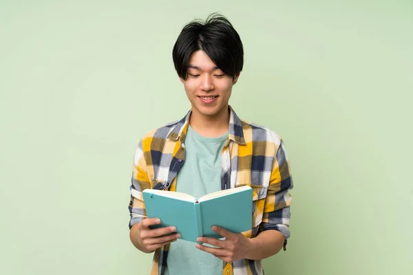 亚洲男子在孤立的绿色墙举行和阅读一本书 — 图库照片