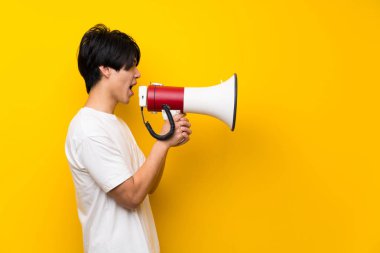Bir megafon ile bağırarak izole sarı duvar üzerinde Asyalı adam