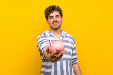 Sarı duvar üzerinde bir kumbara tutan sarışın adam