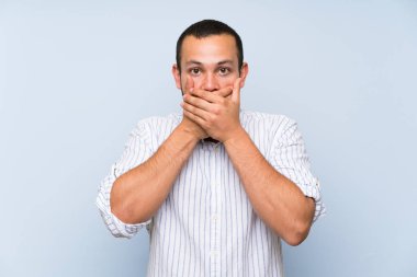 Elleri ile ağız kapsayan izole mavi duvar üzerinde Kolombiyalı adam
