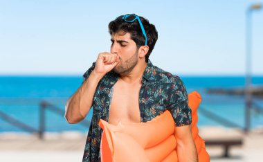 Şortlu adam öksürük çekiyor ve plajda kendini kötü hissediyor.