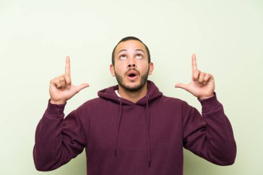 Yeşil duvar üzerinde Sweatshirt ile Kolombiyalı adam indeks parmak büyük bir fikir ile işaret