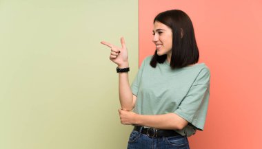 Izole renkli duvar tarafında parmak işaret genç kadın