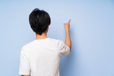 İzole mavi arka plan üzerinde Asyalı adam işaret parmağı ile geri işaret