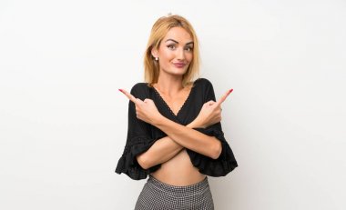 İzole edilmiş beyaz duvarın üzerindeki genç sarışın kadın, yan taraftaki kuşkuları işaret ediyor.