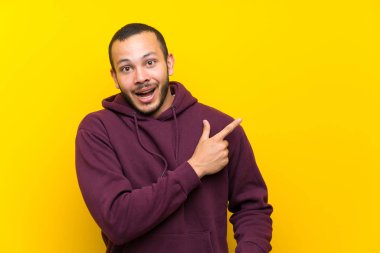 Sarı duvar üzerinde sweatshirt ile Kolombiyalı adam şaşırttı ve yan işaret