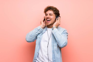 Sarışın adam pembe duvar üzerinde kulaklık ile müzik dinlerken