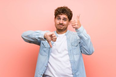 Pembe duvarın üstündeki sarışın adam iyi-kötü işareti yapıyor. Evet ya da değil arasında kararsız