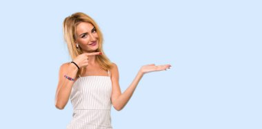 İzole mavi arka plan üzerinde bir reklam eklemek için avuç üzerinde copyspace hayali tutan genç sarışın kadın