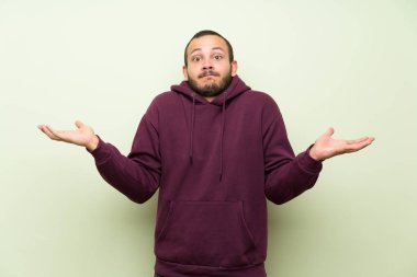 Yeşil duvara Sweatshirt ile Kolombiyalı adam yüz ifade şaşırtmak ile şüphe var