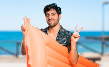 Plajda iki eliyle zafer işareti gösteren şortlu adam