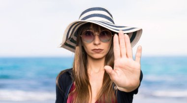 Bikinili genç bir kadın kumsalda eli ile jest yapmayı kesiyor.