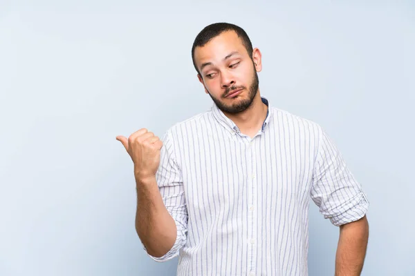 Hombre Colombiano Sobre Aislado Muro Azul Infeliz Señalando Hacia Lado —  Fotos de Stock