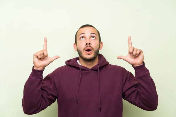 Hombre Colombiano Con Sudadera Sobre Pared Verde Señalando Con Dedo —  Fotos de Stock