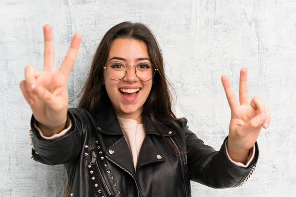 Genç kız grunge duvar üzerinde gülümseyerek ve zafer işareti gösteren