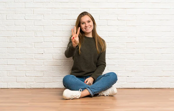 Νεαρή Γυναίκα Κάθεται Στο Πάτωμα Χαρούμενη Και Μετράει Τρία Δάχτυλα — Φωτογραφία Αρχείου
