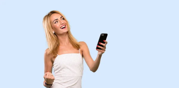 Junge Blonde Frau Mit Handy Siegesposition Vor Isoliertem Blauen Hintergrund — Stockfoto