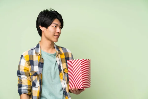 亚洲男子在孤立的绿色墙上拿着一碗爆米花 — 图库照片