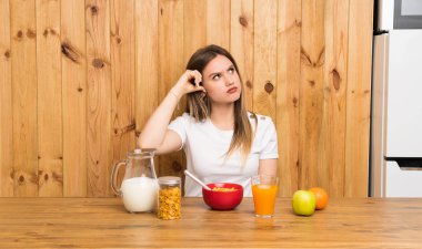 Genç sarışın kadın kahvaltı yapıyor, kuşkuları var ve kafası karışmış bir ifadeyle.