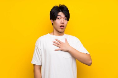 Izole sarı duvar üzerinde Asyalı adam şaşırttı ve doğru bakarken şok