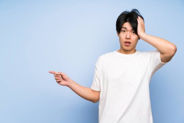 Izole mavi arka plan yan parmak işaret ve bir ürün sunan Asyalı adam