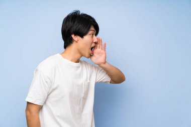 Ağzı tamamen açık diye bağıran izole mavi arka plan asyalı adam