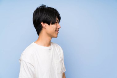 Izole mavi arka plan üzerinde Asyalı adam ayakta ve yan bakıyor