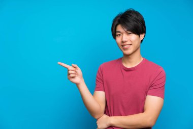 Izole mavi duvar tarafında parmak işaret üzerinde kırmızı gömlekli Asyalı adam