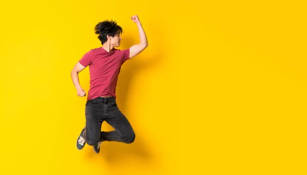 Asiatico uomo jumping oltre isolato giallo muro — Foto Stock