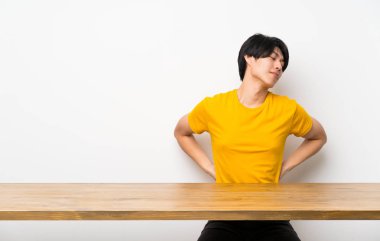 Sarı gömlekli Asyalı adam çaba sarf etmiş olduğu için sırt ağrısı çekiyor