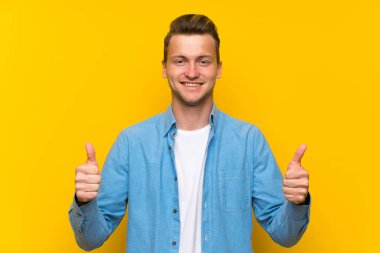 Sarışın yakışıklı adam üzerinde izole duvar veren bir thumbs yukarı jest
