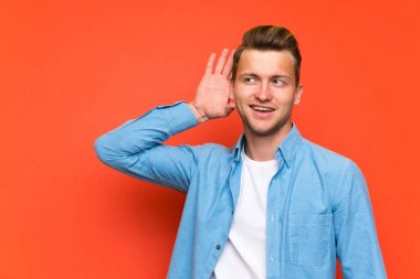 Sarışın yakışıklı adam izole duvar üzerinde bir şey dinlerken