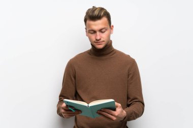 Bir kitap tutan izole beyaz duvar üzerinde Blonde adam ve okuma zevk