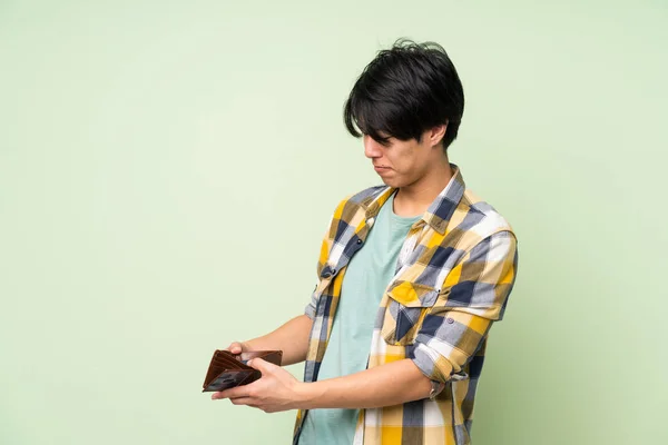Asian man over isolated green wall holding a wallet