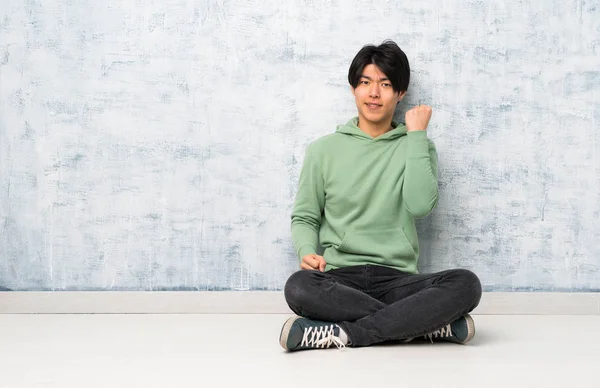 Asian man sitting on the floor with angry gesture