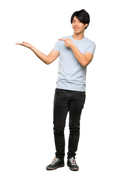 孤立した白い背景の上に広告を挿入するために 手のひらにコピースペースの架空を保持する青いシャツを持つアジア人男性のフルレングスショット — ストック写真