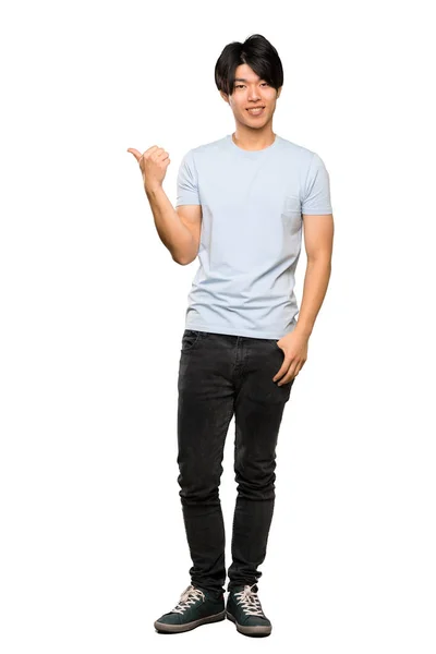 青いシャツを着たアジア人男性が 孤立した白い背景の上に製品を提示する側面を指し示すフルレングスショット — ストック写真