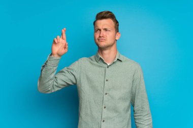Parmaklar geçiş ve en iyi isteyen ile izole mavi duvar üzerinde sarışın adam