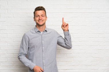 Beyaz tuğla duvar üzerinde Blonde adam gösteren ve en iyi işareti bir parmak kaldırma