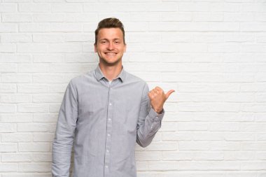 Bir ürün sunmak için yan işaret beyaz tuğla duvar üzerinde Blonde adam