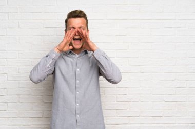 Beyaz tuğla duvar üzerinde Blonde adam bağırarak ve bir şey ilan