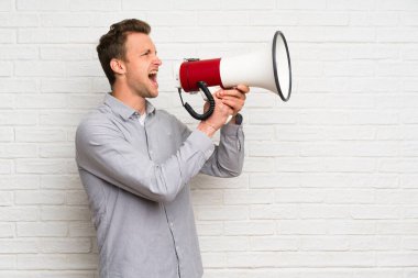 Beyaz tuğla duvar üzerinde Sarışın adam bir megafon ile bağırıyor