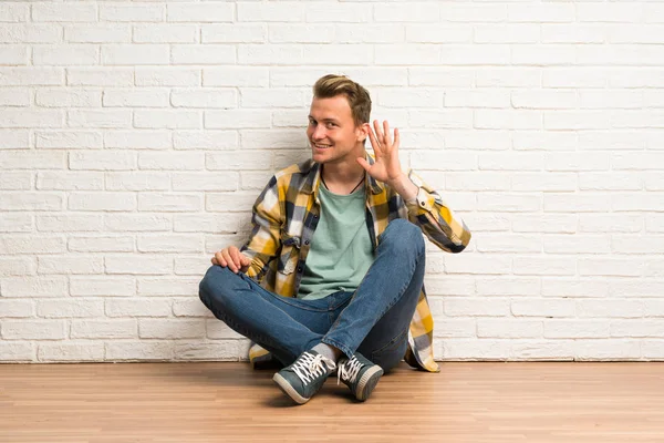 Ξανθός Άνθρωπος Κάθεται Στο Πάτωμα Ακούγοντας Κάτι Βάζοντας Χέρι Στο — Φωτογραφία Αρχείου