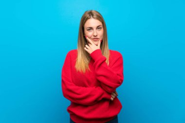 Mavi duvar düşünme üzerinde kırmızı kazaklı kadın